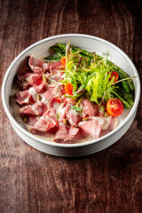 vibrant bowl of fresh salad featuring sliced meat, cherry tomatoes, greens, and creamy dressing, all set on rustic wooden table. Perfect for healthy eating and culinary presentations. vitello tonnato