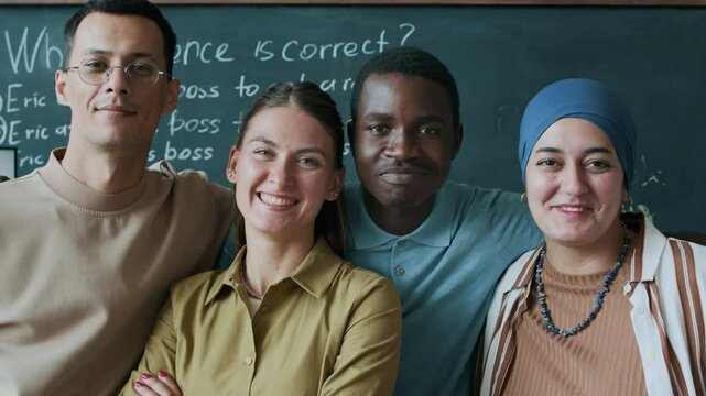 Waist up slowmo portrait of multiracial group of young adult male and female students standing against blackboard with sentence correction exercise and smiling at camera