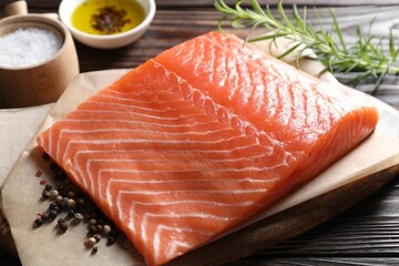 Piece of fresh salmon and spices on wooden table, closeup