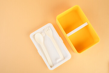 Plastic lunch box with cutlery on peach background, top view