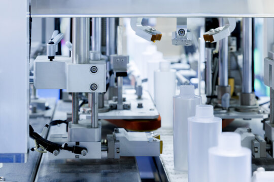 robot arm moving plastic bottle to conveyor belt of auto capping and labeling machine at cosmetic and skin care manufacturing. cosmetic industry and ai technology machinery concept.