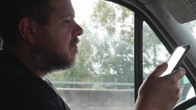 A truck driver with short hair uses his smartphone while driving, posing a significant danger by not watching the road. This risky behavior highlights the hazards of distracted driving.