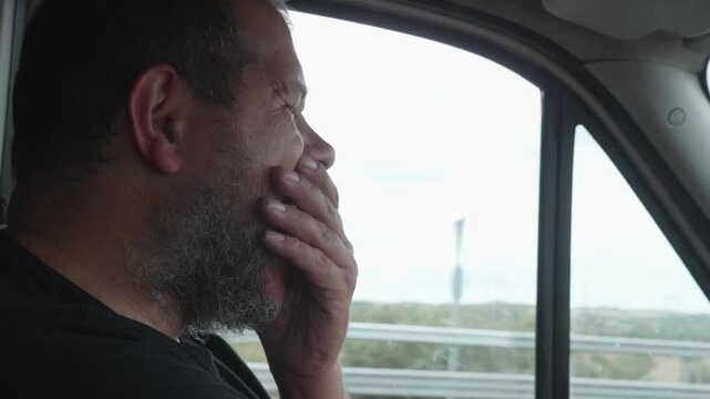 A truck driver with short hair yawns due to fatigue and sleepiness while driving. This dangerous behavior underscores the risks of driving while tired.