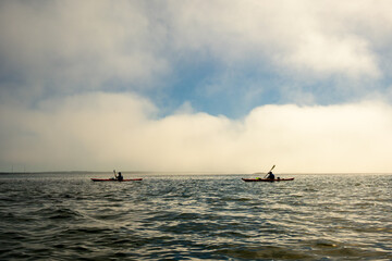 Fototapeta premium Sea kayakers paddle across frame from right to left in front of cloud bank on Georgian Bay room for text