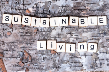 Sustainable Living, phrase spelled out in block wooden letters, black on white, on wood bark...