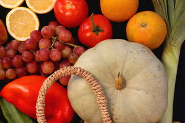 Round straw bag and various seasonal fruits and vegetables on dark background. Summer and fall produce. Top view.