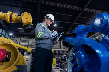 Engineer standing by robotic arm and operating machine in industry factory, technician worker check for repair maintenance electronic operation