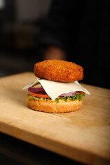 Stop motion of assembling burger. burber bon a chopping wood with Lettuce, tomatoes, onion, cheese and veg patty on it.