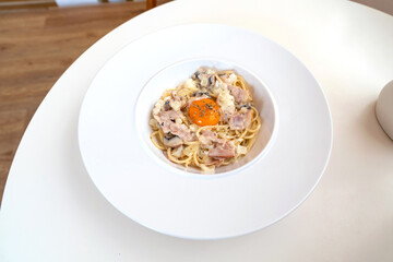 Spaghetti carbonara with Onsen Egg in a white plate on a table in cafe restaurant.