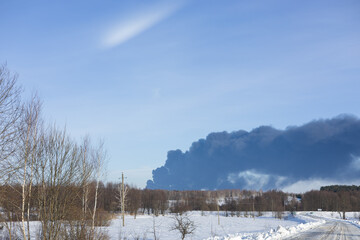 Black smoke rises above the horizon on a clear winter day, creating a sharp contrast with the blue sky. Thick smoke from a severe fire in the forest. Accident and fire.