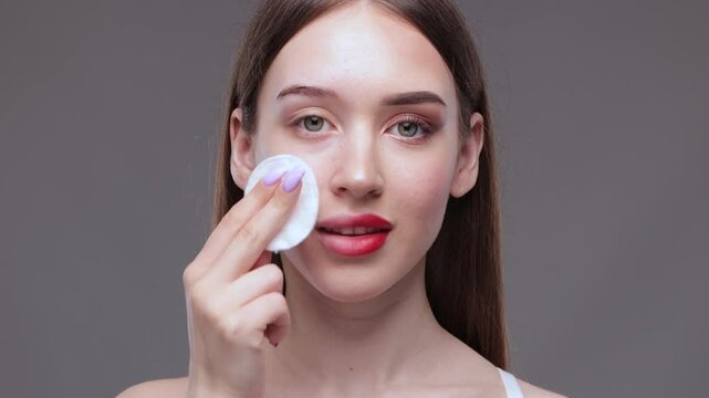 A young beautiful girl removes makeup with a cotton pad and micellar water from her face and eyes.
