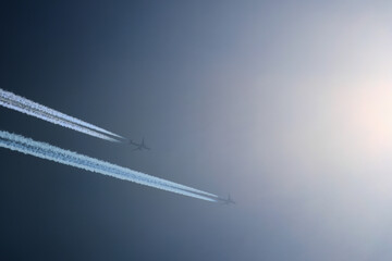 Two planes are flying towards the sun. Airplanes in the blue sky. Airplane with contrail.