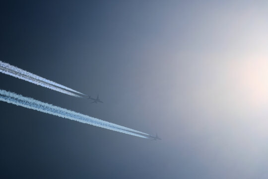 Two planes are flying towards the sun. Airplanes in the blue sky. Airplane with contrail.