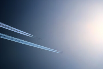Two planes are flying towards the sun. Airplanes in the blue sky. Airplane with contrail.