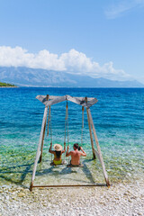 A couple enjoys a tranquil moment while swinging by the shoreline, surrounded by the stunning turquoise sea and mountain views of Brac Island, capturing the essence of a summer getaway.