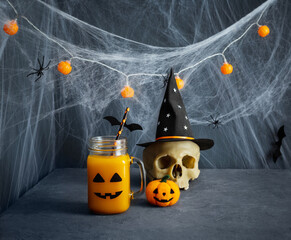 Halloween party decorations. Pumpkin juice with scary face, cobwebs and skull on blue background. Halloween drink.