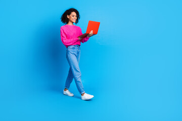 Full size photo of pretty young girl walk hold netbook wear trendy pink outfit isolated on blue color background