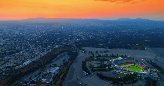 Panorama of Los Angeles with Dodgers Stadium. Orange sky above the rocky horizon at backdrop. Aerial view.