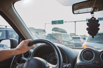 A car is stuck at the border due to the traffic jam, hot summer day, a lot of cars around, a hand is visible resting on a steering wheel