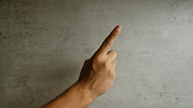 Man pointing with finger towards concrete wall, displaying hand gesture against textured gray surface, highlighting human expression and interaction