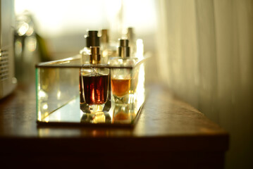 perfume bottles on a glass tray, seen on a wooden dresser by a window filled with sunlight