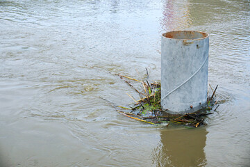Pipe barrier, partially submerged in water with debris accumulated around its base, potential...