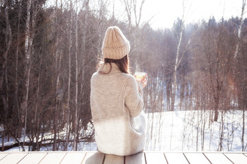 Pensive woman looking on winter forest sitting alone drinking hot tea in cold sunny winter day...
