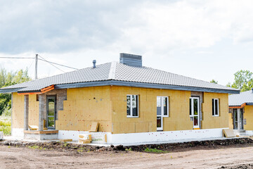 A bright yellow house is currently under construction in a large dirt field, surrounded by the...