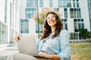Fototapeta premium Young businesswoman is working on laptop in front of modern building