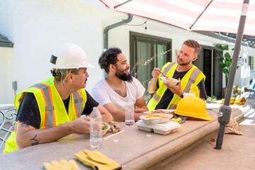 During a sunny lunch break on a project, diverse construction workers and an architect share...