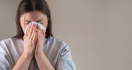 Young brunette woman closes her eyes and blows her nose, dealing with nasal congestion from...