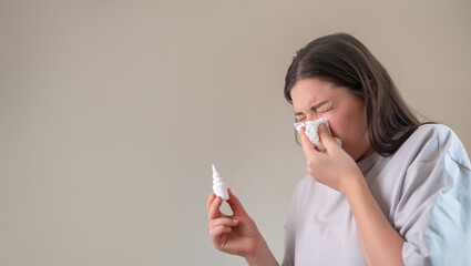 Nasal hygiene with spray, girl clears nasal passages by blowing into a tissue, holding a nasal spray for congestion relief.