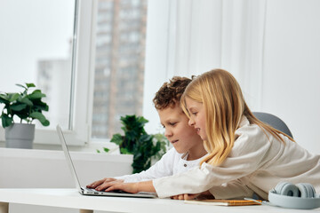 Happy siblings studying at home on laptops for their online elearning lessons The boy and girl are sitting at a table in their cozy living room, concentrating with headphones on The background shows