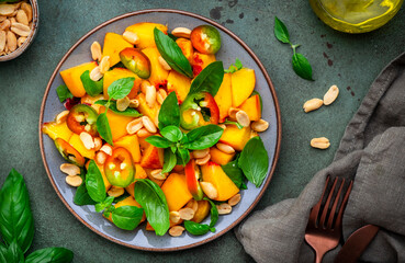 Foodie food salad with peach, hot chili peppers, peanuts and basil, green background, top view