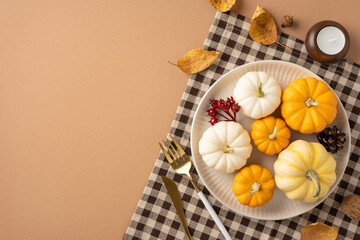 Overhead view of a Thanksgiving table setup featuring small pumpkins, autumn leaves, and a checkered cloth, representing the essence of fall and celebration
