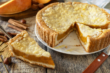 Fall traditional pumpkin pie with cinnamon on a rustic wooden background.