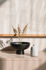 Composition with dried twigs in a vase, ceramics on a sideboard in a living room.