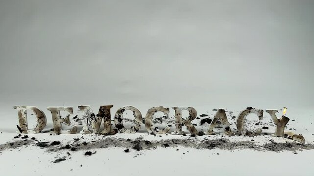Wooden letters spelling out democracy burn against white seamless background