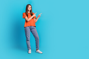 Full length photo of lovely teen lady point empty space dressed stylish orange garment isolated on blue color background