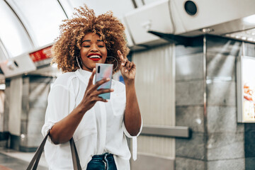 Beautiful fashionable black woman standing at a subway train station. She is happy and talking to...