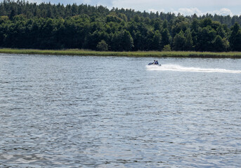 A speedboat gliding across a serene lake surrounded by lush green forests, capturing the thrill of summer adventures on water.