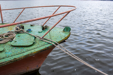 Obraz premium A close-up of an old, weathered boat resting on the water, showcasing its vibrant green paint and rusty metal details. The tranquil water reflects the boat’s unique colors.
