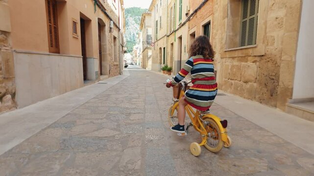 Young girl riding a tricycle down a quaint European street