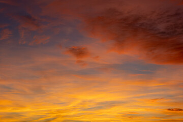 The sky is ablaze with vibrant orange and purple hues as the sun sets below the horizon, casting a warm glow on the wispy clouds