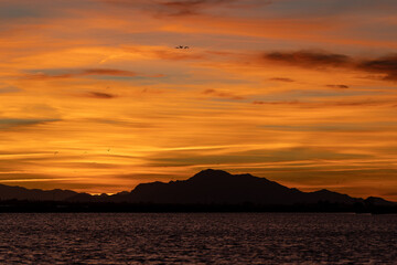 The sun sets. Painting the sky in fiery shades over a serene lake and majestic mountains. With birds soaring gracefully through colorful clouds