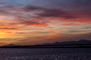 The stunning sunset reflects colorful hues on a calm lake, with majestic mountains in the distance. Perfect for nature lovers seeking a serene landscape