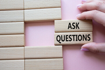 Ask Questions symbol. Wooden blocks with words Ask Questions. Businessman hand. Beautiful pink...