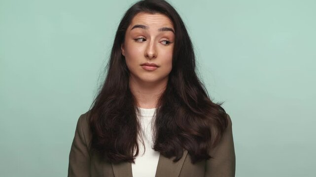 Portrait of a young woman with a look of contempt, expressing discontent against a teal background.