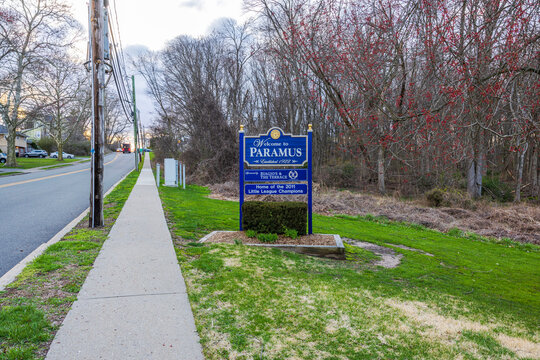 Welcome to Paramus sign on early spring street in New Jersey with asphalt road, villas, parked cars, and bare trees. New Jersey, USA. 