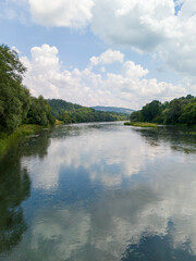 Fototapeta premium A serene river view reflecting clouds and lush greenery, perfect for invoking tranquility and nature's beauty.
